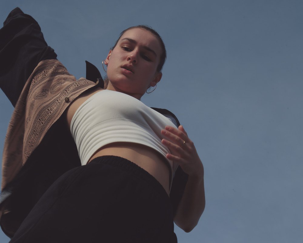 A dancer against blue sky, one arm stretched overhead, face turned upward.