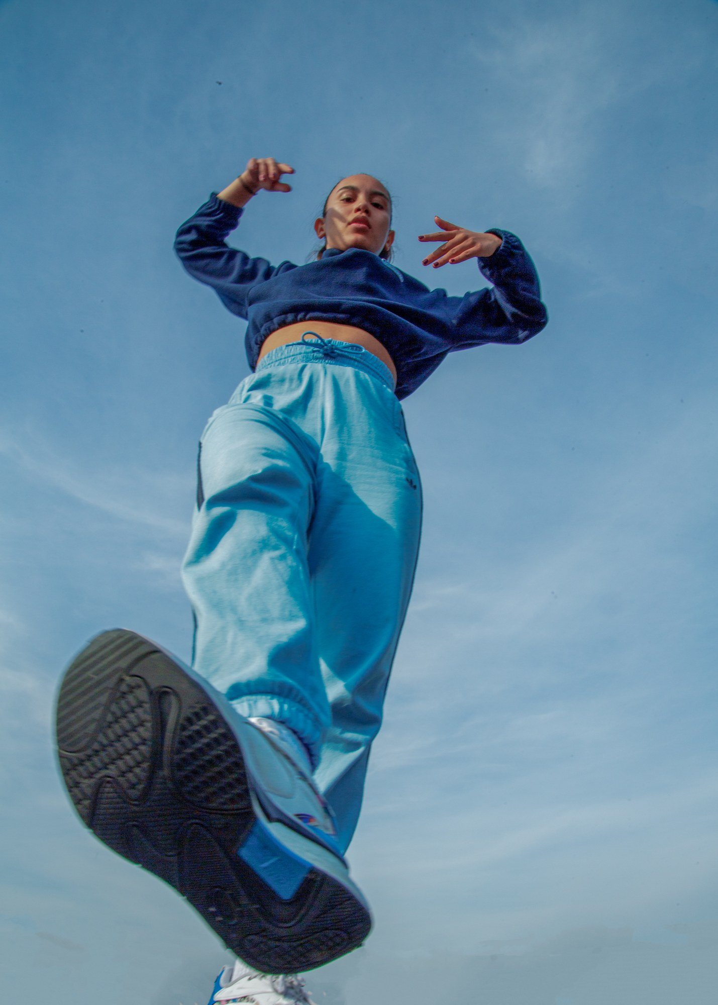 A dancer in a blue sweatshirt and pale jeans suspended mid-jump against clear sky.
