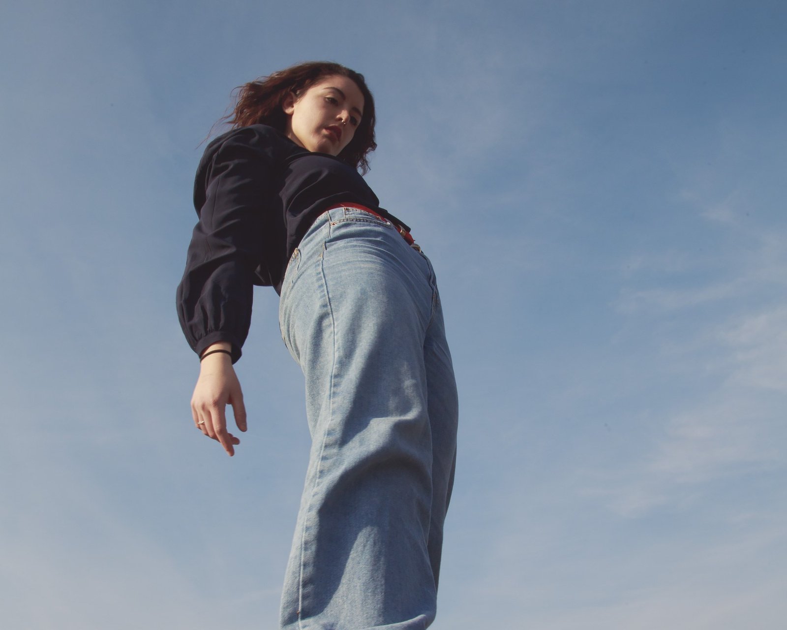 A dancer in wide light denim jeans and a navy blouse, one hand hanging loose.