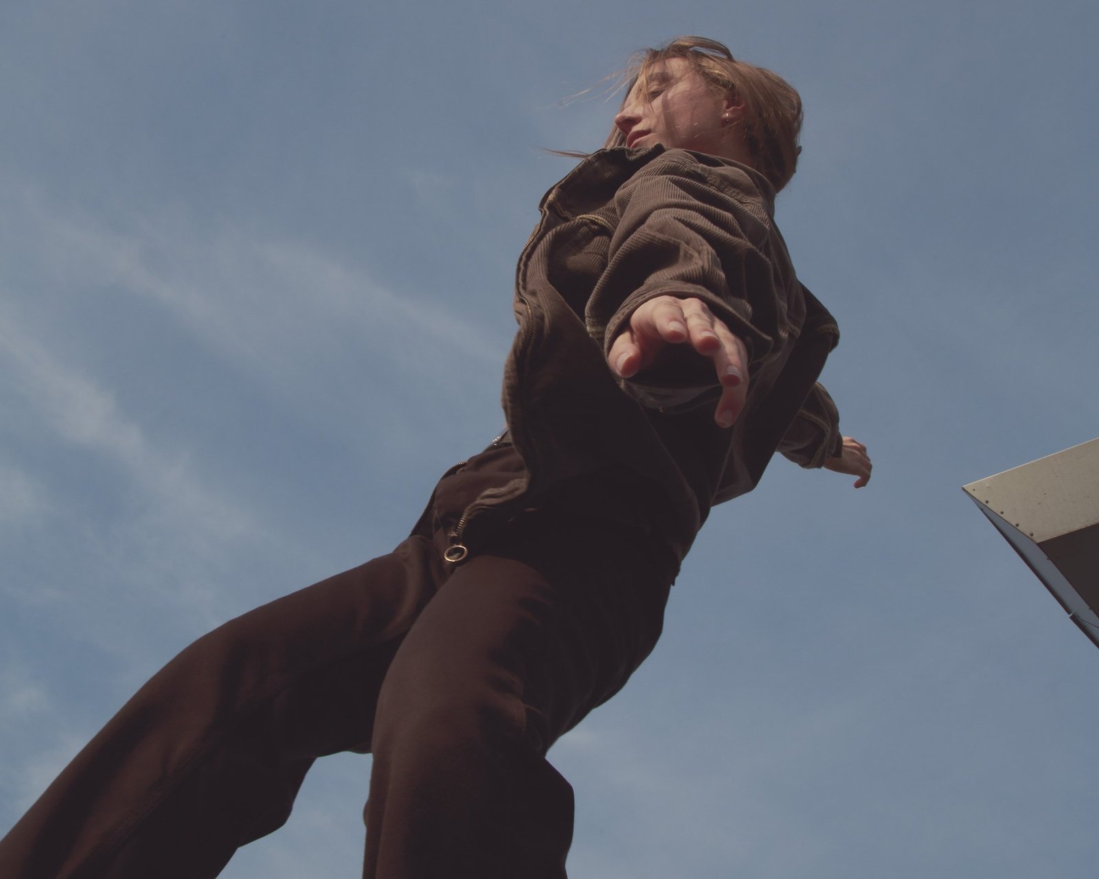 A dancer in a brown corduroy jacket reaching one hand directly toward the camera.