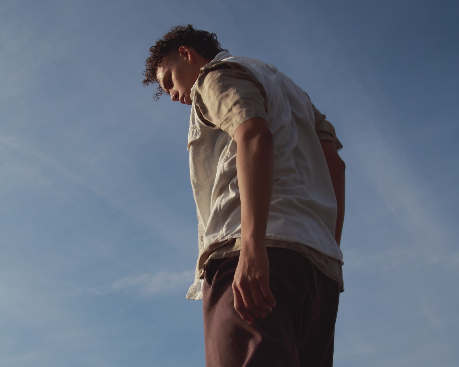 A dancer in a pale shirt, head lowered, shoulders turned away, sunlight across the face.