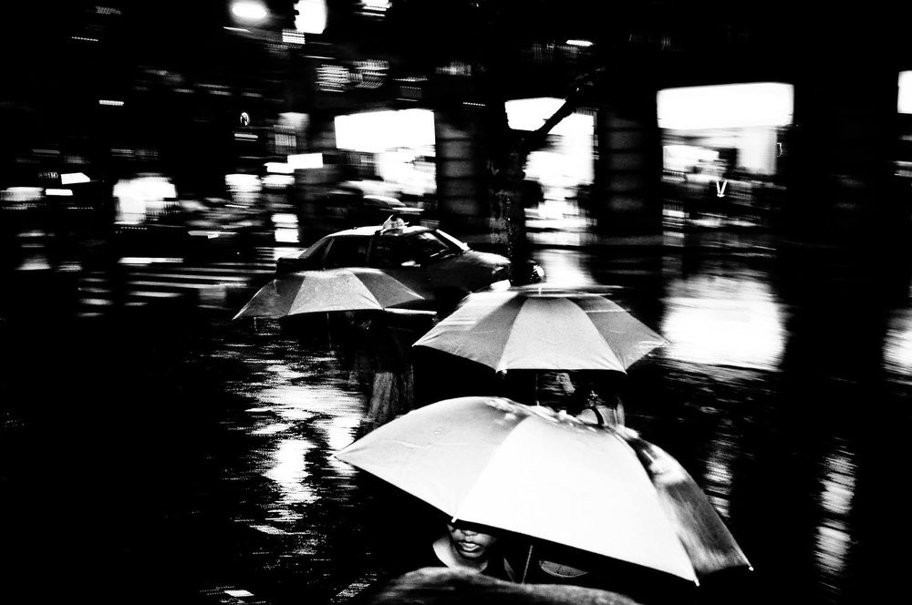 Paper umbrellas glowing over a wet street at night, light reflected in the road.