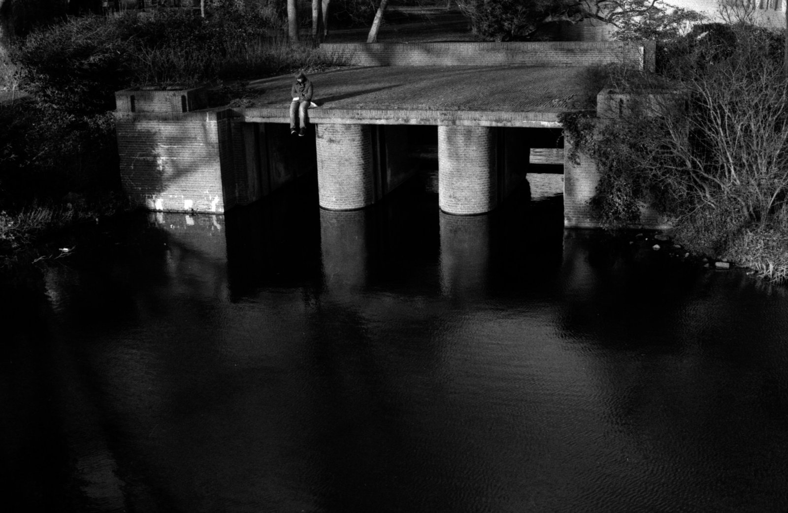 A low bridge over black water at night, its piers doubled in the reflection.