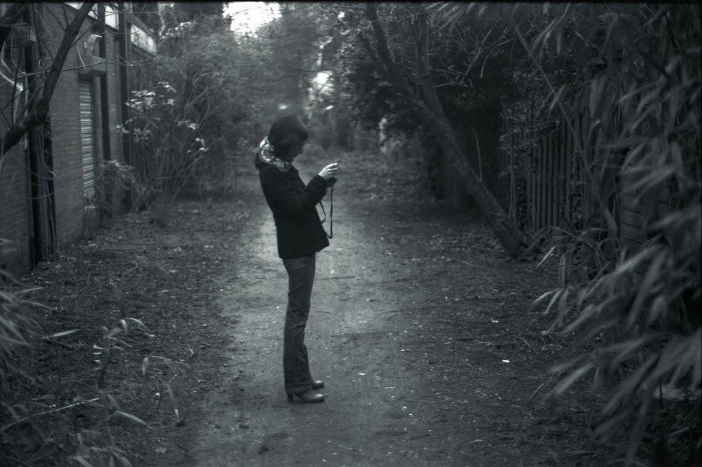 A figure standing alone in a dark lane, raising a camera.