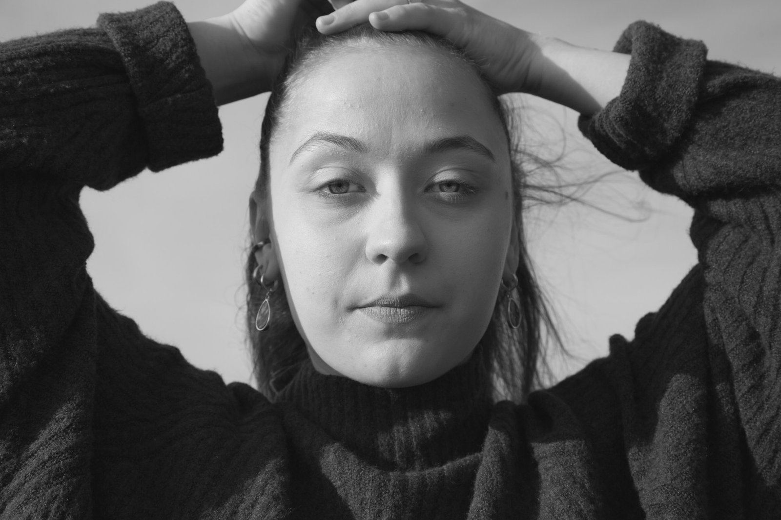 A woman in a heavy wool sweater, both hands resting on top of her head.