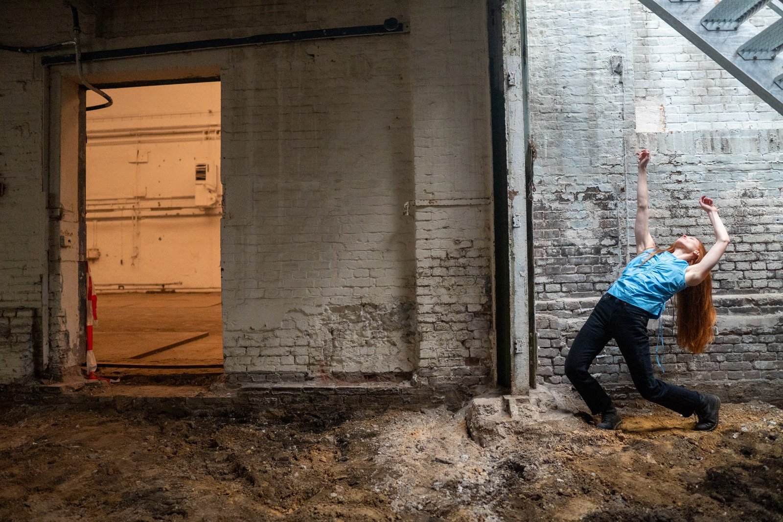 Two frames: an orange-lit doorway in a stripped interior, and a dancer on rubble against the city.