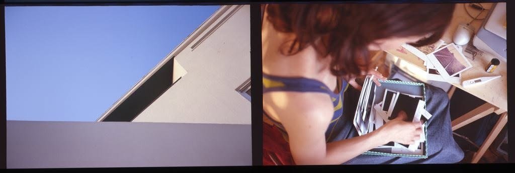 A building corner against blue sky beside a woman sorting photographs at a desk.