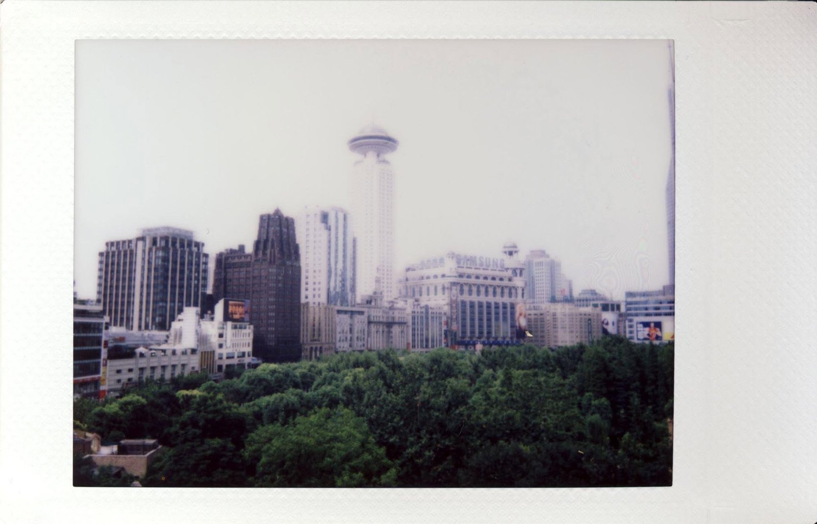 The Shanghai skyline seen over dense treetops, hazy and overexposed.
