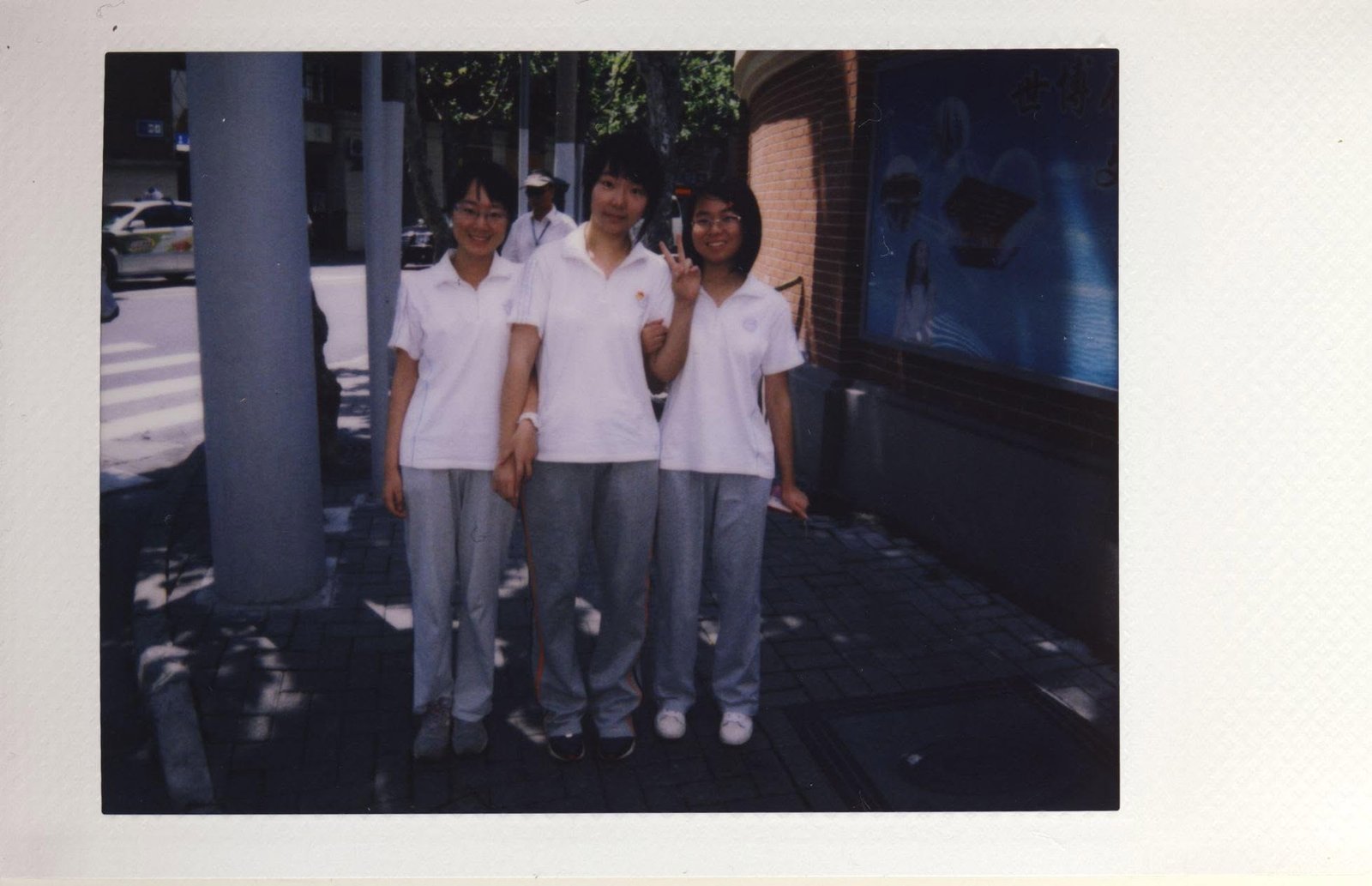 Three schoolgirls in white uniforms beside a pillar, one making a peace sign.
