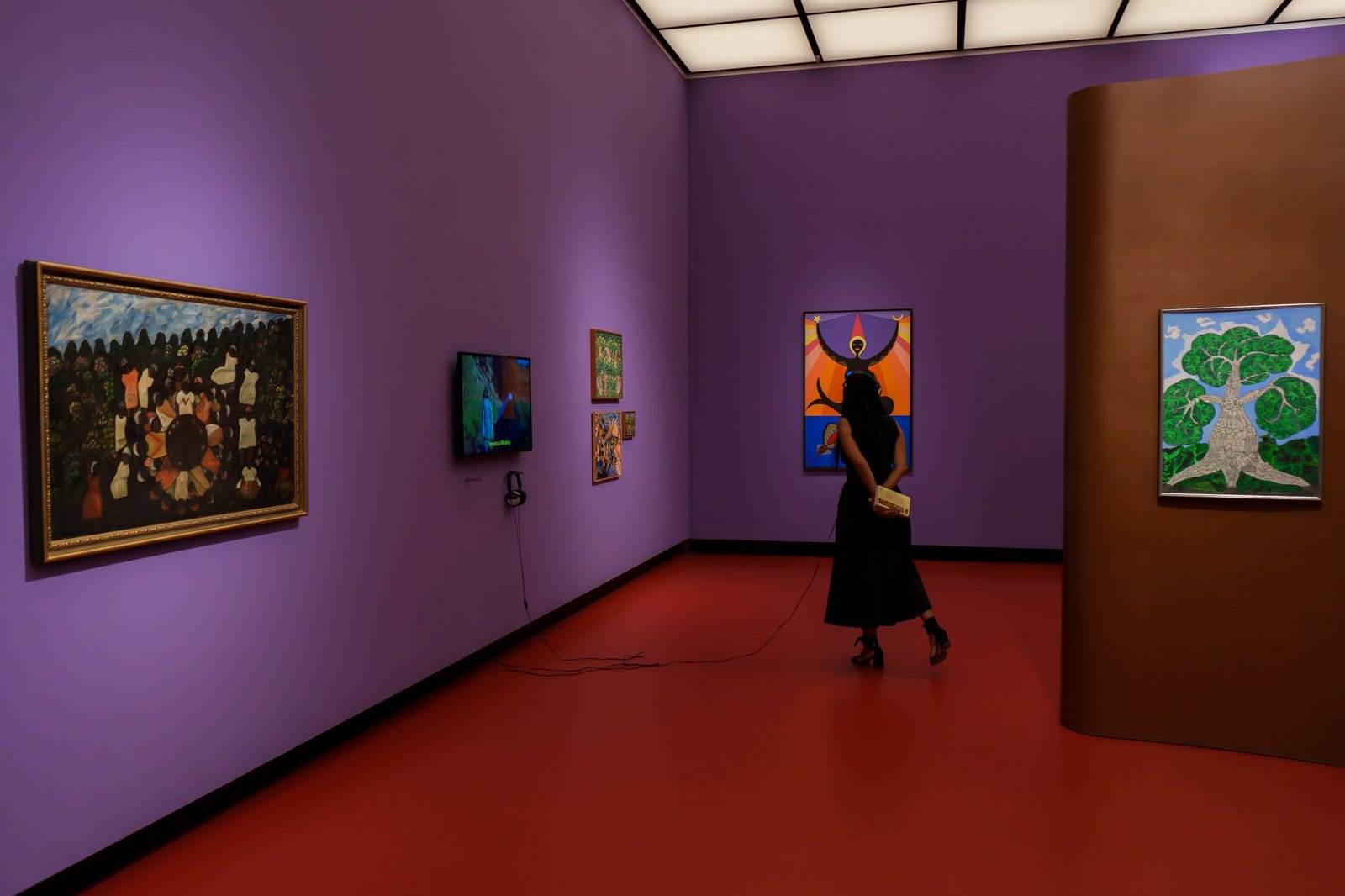 A museum gallery with violet walls and a red floor, one visitor walking the length of it.